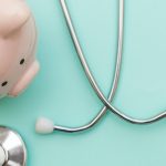 Stethoscope on table next to piggy bank